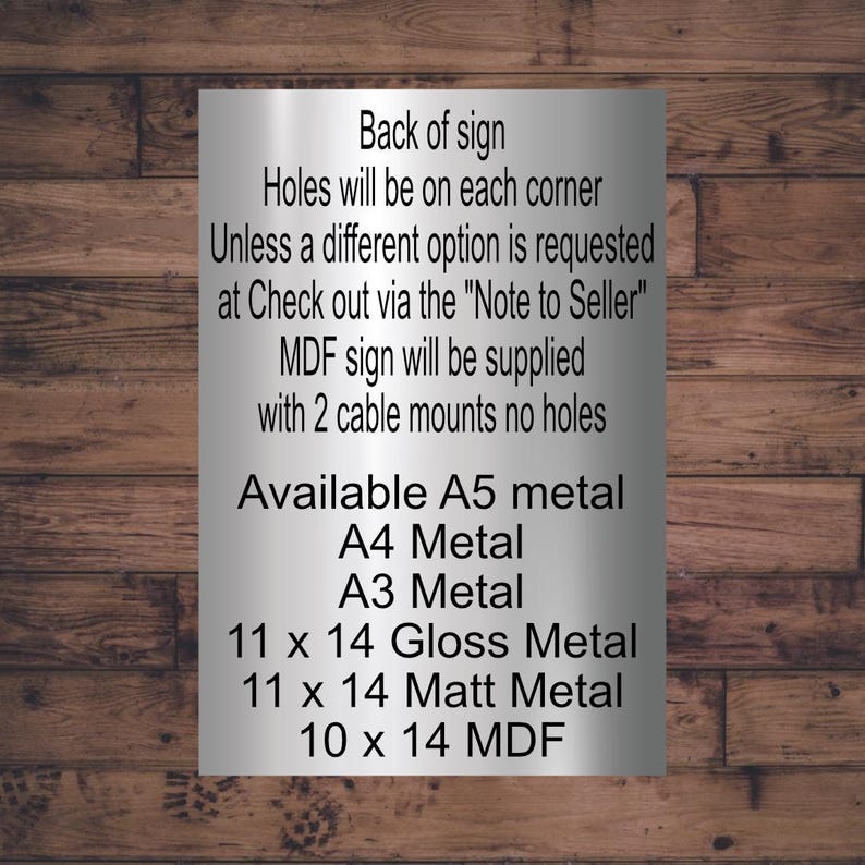 May include: A silver metal sign with black text on a wooden background. The text includes information about the sign's back, hole options, and available sizes: A5, A4, A3, 11 x 14 inch gloss and matt metal, and 10 x 14 MDF.