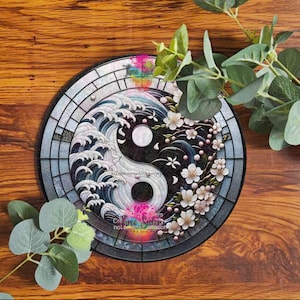 A stained glass yin yang design with a wave pattern on one side and a cherry blossom branch on the other. The design is set in a circular frame with a dark wood background.