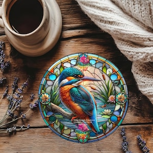 May include: A circular coaster with a stained-glass effect, depicting a kingfisher bird in vibrant colours. The design includes a blue, orange, and green palette, with the text "Three Sisters Creations" visible at the bottom.
