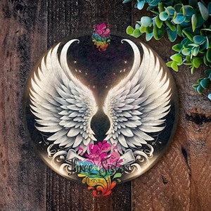 May include: A round, white, wooden sign with a pair of white angel wings in the centre. The wings are outlined in gold and have a black background. The sign has a rainbow floral design around the edges.