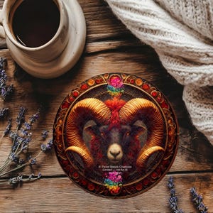 May include: A circular coaster featuring a detailed illustration of a ram's head with large golden horns and a dark face. The coaster has a decorative border with red and gold accents. The text "Three Sisters Creations" is visible.