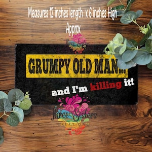Può includere: Un cartello rettangolare con la scritta "GRUMPY OLD MAN... and I'm killing it!" in nero, bianco e rosso. Il cartello misura circa 30 cm di lunghezza e 15 cm di altezza. Lo sfondo è nero con un rettangolo giallo.
