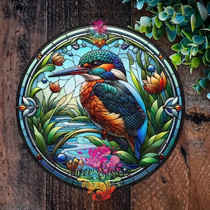 May include: A stained glass style illustration of a blue and green kingfisher perched on a branch with a stream of water below. The background is a blue sky with white clouds. The illustration is surrounded by a circular frame.