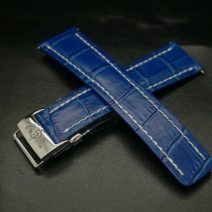 May include: Blue leather watch strap with white stitching and a silver buckle featuring a butterfly logo.