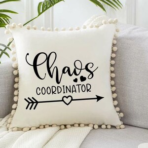 Peut inclure: Un oreiller blanc avec un motif noir et blanc qui dit "Chaos Coordinator" avec une fl&egrave;che et des c&oelig;urs. L'oreiller a une bordure en pompons blancs.
