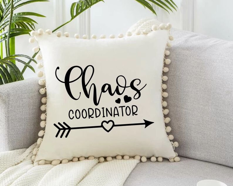 Peut inclure: Un oreiller blanc avec un motif noir et blanc qui dit "Chaos Coordinator" avec une fl&egrave;che et des c&oelig;urs. L'oreiller a une bordure en pompons blancs.