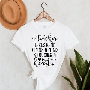 Peut inclure: T-shirt blanc avec un texte noir qui dit "a teacher takes hand opens a mind & touches a heart" avec quatre petits c&oelig;urs noirs.