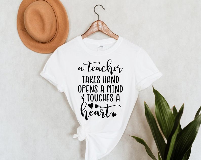 Peut inclure: T-shirt blanc avec un texte noir qui dit "a teacher takes hand opens a mind & touches a heart" avec quatre petits c&oelig;urs noirs.