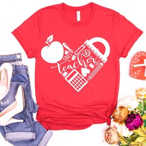 Peut inclure: T-shirt rouge avec un motif de c&oelig;ur blanc repr&eacute;sentant le mot "Teacher" et des fournitures scolaires comme une r&egrave;gle, un crayon et une calculatrice.