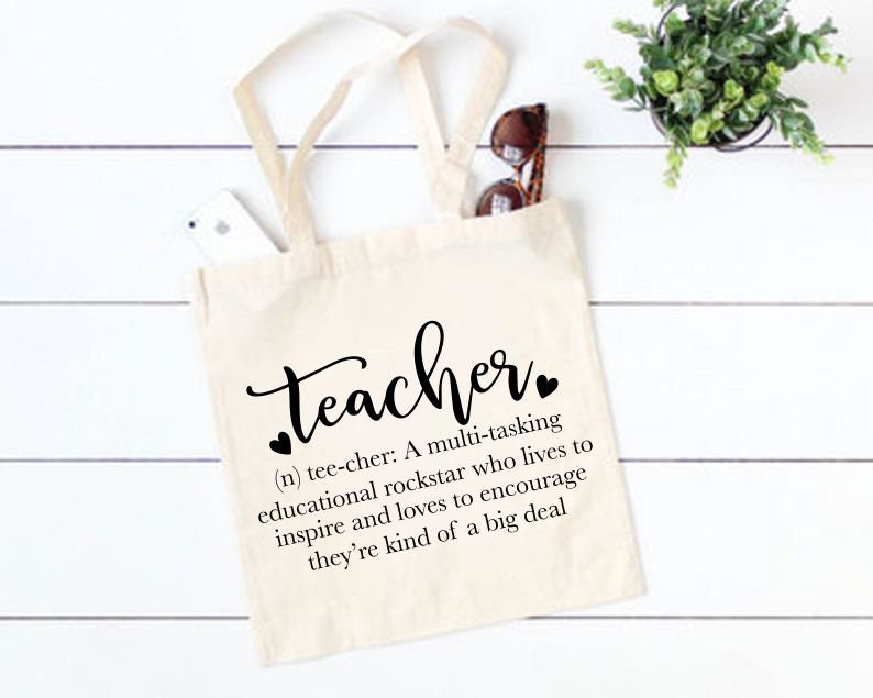 Peut inclure: Un sac fourre-tout blanc avec du texte noir qui dit "teacher" et une d&eacute;finition du mot. La d&eacute;finition se lit comme suit : "(n) tee-cher : Une rockstar multit&acirc;che de l'&eacute;ducation qui vit pour inspirer et aime encourager, c'est un peu un gros probl&egrave;me."