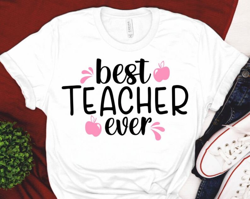 Peut inclure: T-shirt blanc avec le texte "best teacher ever" en lettres noires et un graphique de pomme rose.