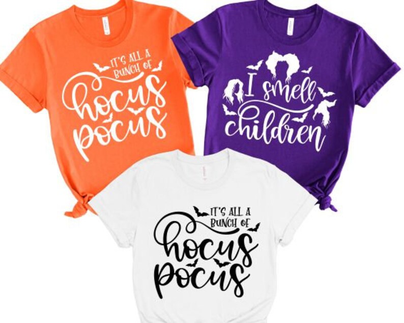 May include: Three t-shirts with Halloween-themed designs. One orange shirt says "It's all a bunch of Hocus Pocus" with bats and a witch's hat. One purple shirt says "I smell children" with bats and a witch's hair. One white shirt says "It's all a bunch of Hocus Pocus" with bats.