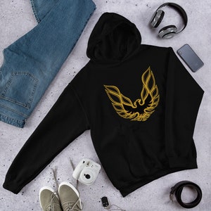 Puede incluir: Sudadera con capucha negra con un logotipo de pájaro bordado en dorado. El logotipo es un pájaro estilizado con las alas extendidas.