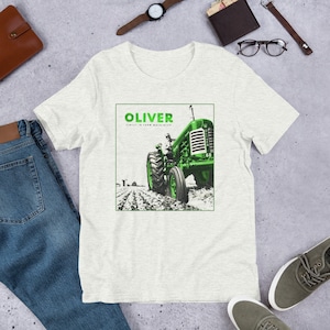 May include: A white t-shirt with a green and black image of an Oliver tractor. The text "Oliver" and "Finest in Farm Machinery" is printed on the shirt.