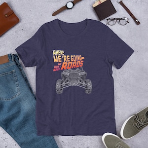 May include: A navy blue t-shirt featuring a graphic of an off-road vehicle and the text "Where We're Going We Don't Need Roads".