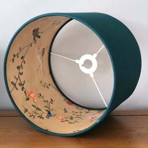 May include: A teal lampshade with a floral and bird design on the inside. The lampshade is made of fabric and has a white metal ring at the top.