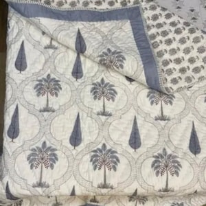 May include: A white cotton quilt with a gray and white pattern of palm trees and stylized trees. The quilt has a blue border.
