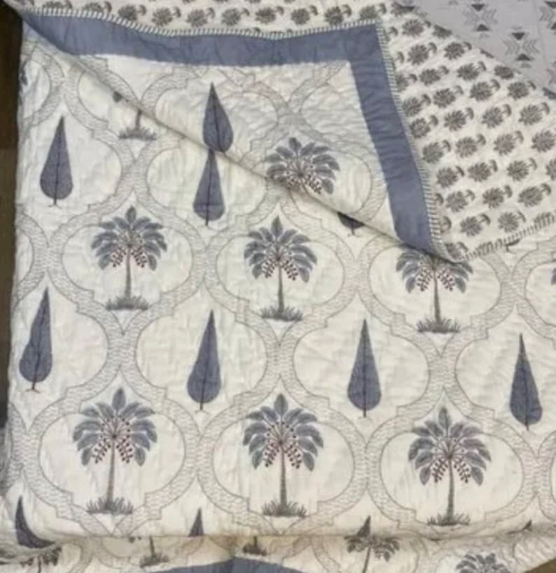 May include: A white cotton quilt with a gray and white pattern of palm trees and stylized trees. The quilt has a blue border.