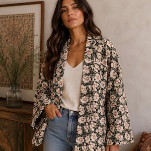 May include: A long-sleeved open-front jacket featuring a dark green base with a repeating light pink floral pattern, worn over a cream-coloured v-neck camisole and light blue denim jeans. The jacket has a relaxed fit with wide sleeves.