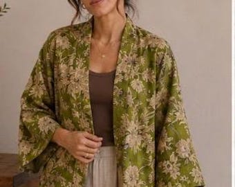 Peut inclure: Une veste kimono vert olive ouverte sur le devant, ornée d'un motif floral répétitif dans des tons beige clair. Le vêtement présente des manches larges trois-quarts et une coupe droite et décontractée portée sur un débardeur marron uni.
