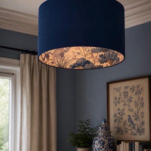 May include: A cylindrical pendant light fitting featuring a solid dark navy blue exterior fabric shade. The interior lining of the drum shade displays a detailed botanical and bird pattern in shades of blue and white, visible from below.