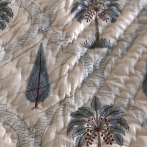May include: White cotton fabric with a repeating pattern of blue and red palm trees and pine trees. The fabric has a quilted texture.