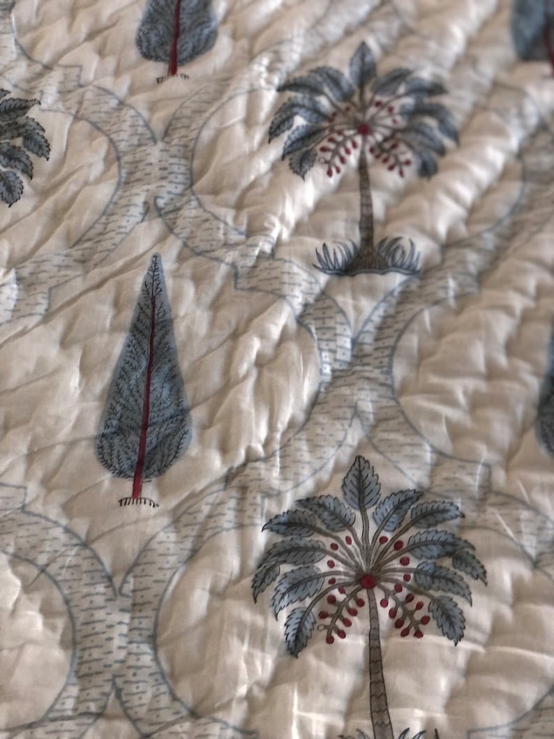 May include: White cotton fabric with a repeating pattern of blue and red palm trees and pine trees. The fabric has a quilted texture.