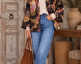 Peut inclure: Une veste noire ouverte à l'avant avec un imprimé floral et botanique multicolore, portée sur un pull en maille crème et un jean bleu. La tenue est complétée par des bottines en daim marron et un sac cabas en daim marron assorti.