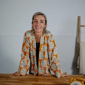 May include: An open-front jacket in a vibrant mustard yellow hue featuring a repeating white and muted green floral block print pattern, long sleeves, and a straight hemline, paired with a solid black top underneath and a vintage yellow rotary phone.