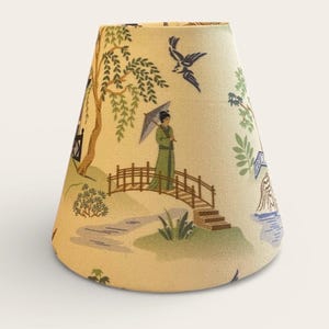 May include: A tapered fabric lampshade with a cream background featuring a printed scene of a person in a green robe holding an umbrella on a wooden bridge, surrounded by willow trees, birds, and water elements in shades of green, blue, and brown.