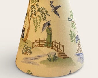 May include: A tapered fabric lampshade with a cream background featuring a printed scene of a person in a green robe holding an umbrella on a wooden bridge, surrounded by willow trees, birds, and water elements in shades of green, blue, and brown.