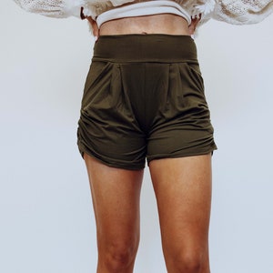 May include: A pair of olive green, high-waisted,  short shorts with a relaxed fit. The shorts have a wide waistband and a slightly gathered look.