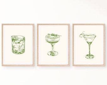 Pode incluir: Três impressões artísticas emolduradas com desenhos a traço verde de coquetéis. As impressões retratam um coquetel em um copo old-fashioned com limão, uma taça com azeitonas e um martini com raspas de limão. As molduras são marrons claras.