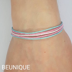 May include: A bracelet made of light blue, pink, and white string. The bracelet is tied in a knot and is worn on a person's wrist.