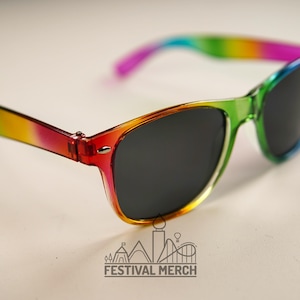 Pode incluir: Óculos de sol de plástico com cores do arco-íris e lentes pretas. Os óculos de sol têm um degradê de cores, começando com vermelho no braço esquerdo e passando para roxo no braço direito.