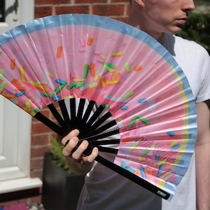 May include: A pink and blue hand fan with a sprinkle pattern. The fan is open and has a black handle with the word "remarkable" printed on it.