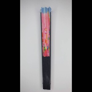 May include: A black folding fan with a pink and blue patterned fabric. The fan is closed and standing upright.
