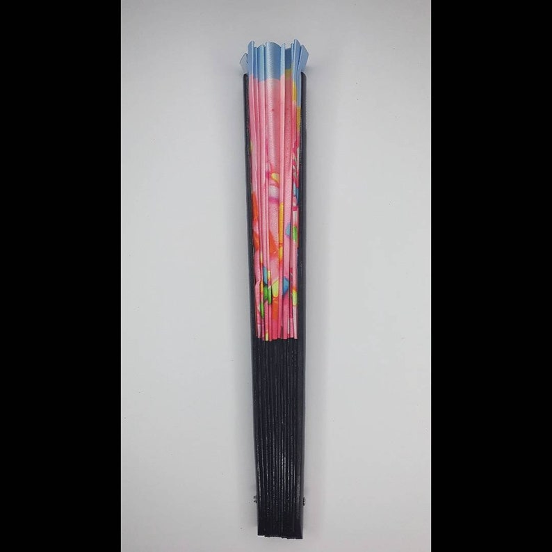 May include: A black folding fan with a pink and blue patterned fabric. The fan is closed and standing upright.
