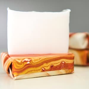 Può includere: Una saponetta bianca si trova su un portasapone decorativo in marmo arancione e marrone.