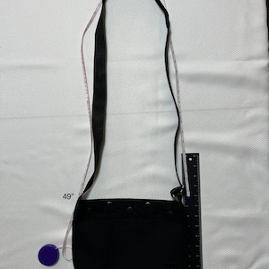 May include: A black crossbody bag with a long adjustable strap. The strap is 49 inches long. The bag has a flap closure and a zipped pocket on the front.