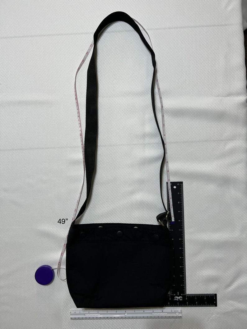 May include: A black crossbody bag with a long adjustable strap. The strap is 49 inches long. The bag has a flap closure and a zipped pocket on the front.