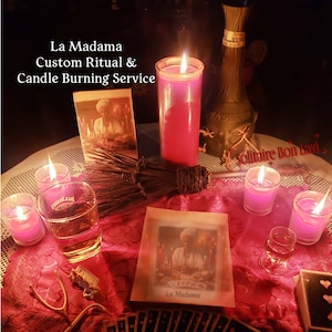 Può includere: Una candela rossa brucia su un tavolo con una tovaglia rossa. Ci sono carte da gioco, un bicchiere di liquido ambrato e un libro con il titolo "La Madamo" sul tavolo. Il testo "La Madamo Custom Ritual & Candle Burning Service" è scritto sopra l'immagine.