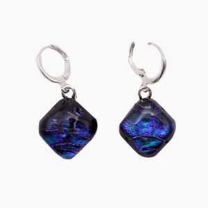May include: A pair of dangle earrings with a silver-tone lever back closure. Each earring features a dark, square-shaped glass bead with iridescent blue and purple hues. The glass has a textured appearance.