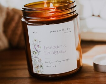May include: A lit, amber-colored glass jar candle with a white label that reads "Lavender & Eucalyptus." The candle is on a wooden tray with a small tea light. The label also says "hand poured soy candle" and "4 oz - 113 g."