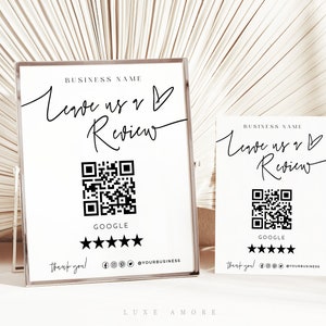 May include: Two white signs with black text and a black and white QR code. The text on the signs reads "Business Name Leave us a Review" with a heart symbol. The signs also include a five-star rating system and the word "Google".