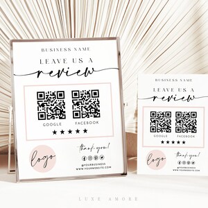 Può includere: Un cartello bianco con testo nero che recita "BUSINESS NAME LEAVE US A review". Sotto il testo ci sono due codici QR in bianco e nero, etichettati come "GOOGLE" e "FACEBOOK". Sotto i codici QR ci sono cinque stelle nere. Un cerchio rosa con la parola "logo" in testo nero si trova nell'angolo in basso a sinistra. Sotto il logo c'è altro testo nero che dice "thank you! @YOURBUSINESS WWW.YOURWEBSITE.COM".