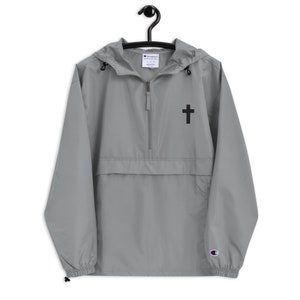May include: A gray Champion brand windbreaker with a black cross embroidered on the front. The jacket has a zipper closure and a hood.