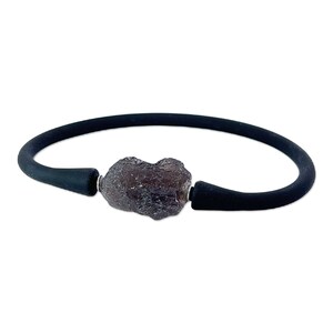 Puede incluir: Una pulsera de goma negra con una piedra preciosa grande, de color gris oscuro, tallada en bruto. La piedra preciosa es el punto focal de la pulsera.