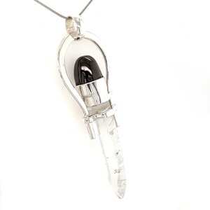 May include: A silver pendant with a clear quartz crystal point and a black gemstone set in a silver cage.