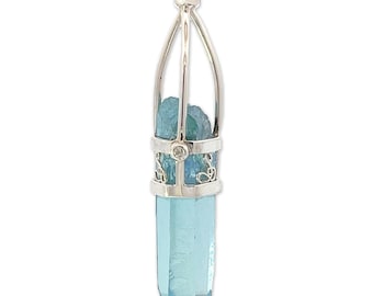 May include: A silver pendant with a blue crystal point encased in a cage-like design. The crystal is a light blue color and has a pointed tip. The pendant is a unique and stylish piece of jewelry.